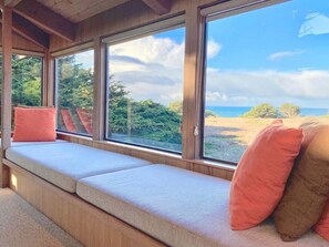 A room with a built-in bench seating area with cushions, large windows offering a view of the outdoors.