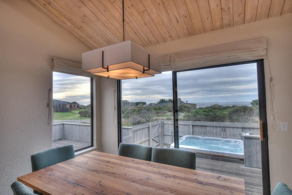 A dining area with a wooden table and chairs, large windows with a view of a backyard and a hot tub.