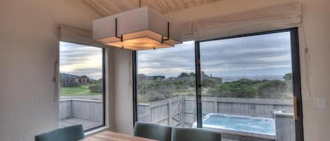 A dining area with a wooden table and chairs, large windows with a view of a backyard and a hot tub.