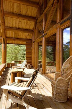 A wooden deck with lounge chairs and a wicker chair, large windows, and a view of greenery. - El Salto Log Home & Guest House wooded setting, hot tub-secluded peaceful (Arroyo Seco)