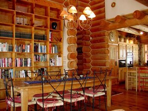 A rustic interior with a wooden bookshelf, a dining table with chairs, and a kitchen area. - El Salto Log Home & Guest House wooded setting, hot tub-secluded peaceful (Arroyo Seco)
