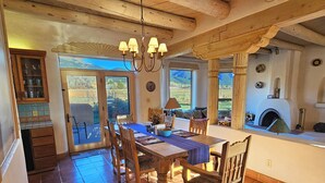 Un espace repas avec une table et des chaises en bois, un lustre et une vue sur l’extérieur grâce à de grandes fenêtres.