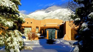 Un bâtiment recouvert de neige, de style architectural traditionnel, entouré d’arbres chargés de neige et avec des montagnes enneigées en arrière-plan.