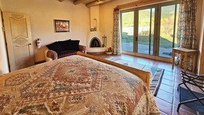 Une chambre spacieuse avec un grand lit, une cheminée et une vue sur l’extérieur grâce à une porte-fenêtre coulissante.