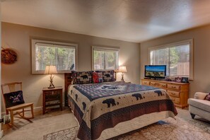 A bedroom with a large bed, two windows, a television, a dresser, and a chair.