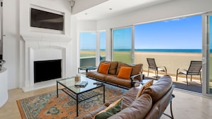 A living room with a fireplace, a sofa, and a large glass door leading to a balcony with a beach view. - 3525O - Big Blue Beauty: 3  BR, 5  BA House in Oxnard, Sleeps 6 (Oxnard)