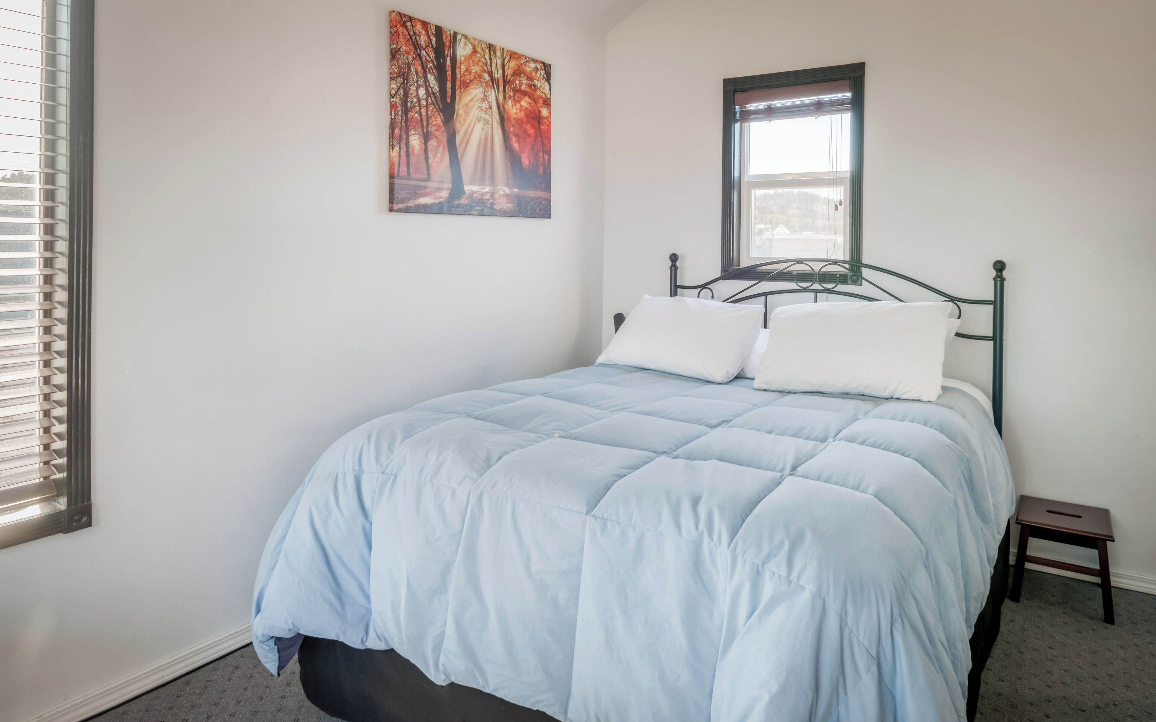 Een slaapkamer met een bed, een raam en een schilderij aan de muur.
