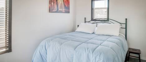 Een slaapkamer met een bed, een raam en een schilderij aan de muur.