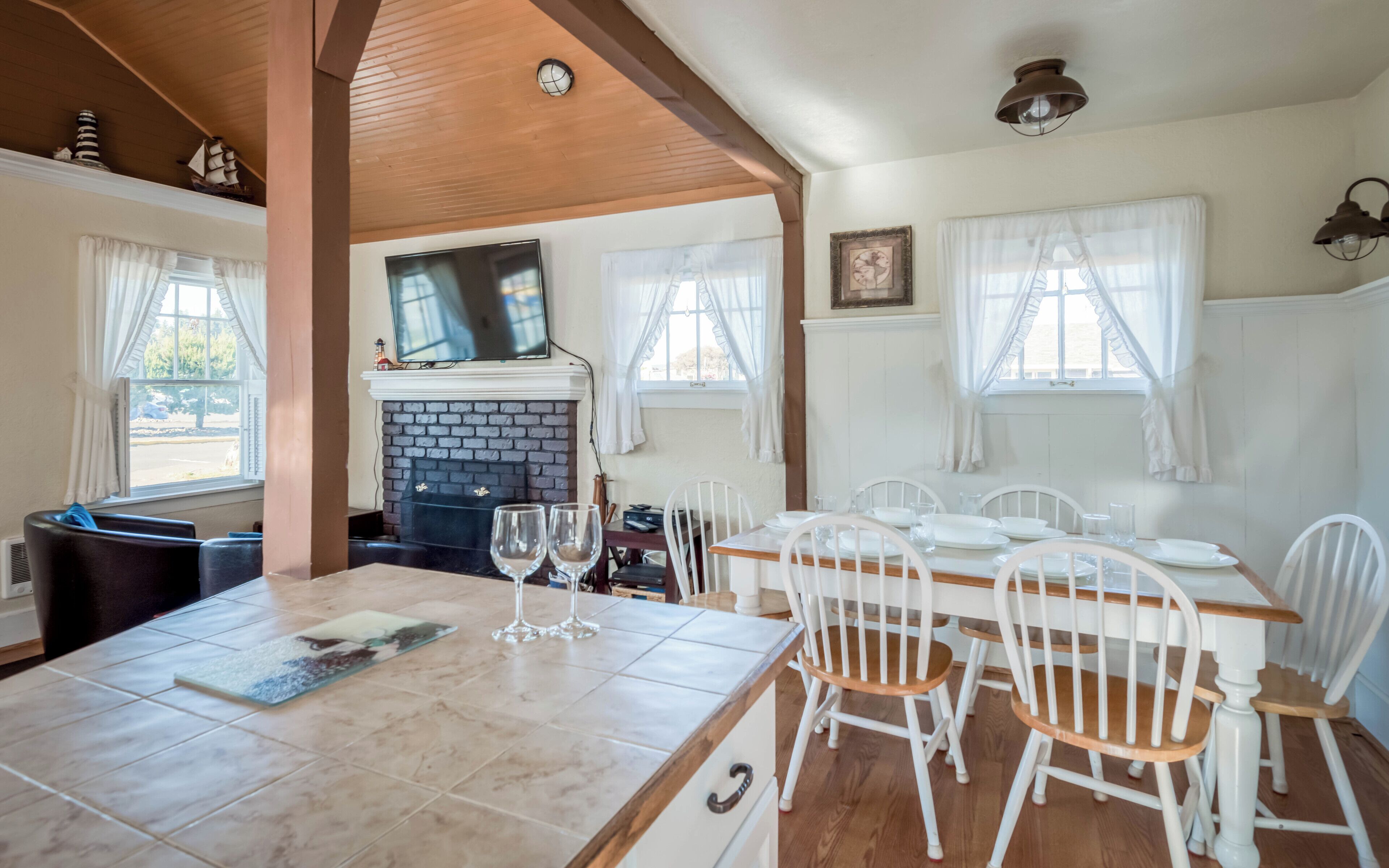 A dining area with a brick fireplace, white chairs, and a tiled table.