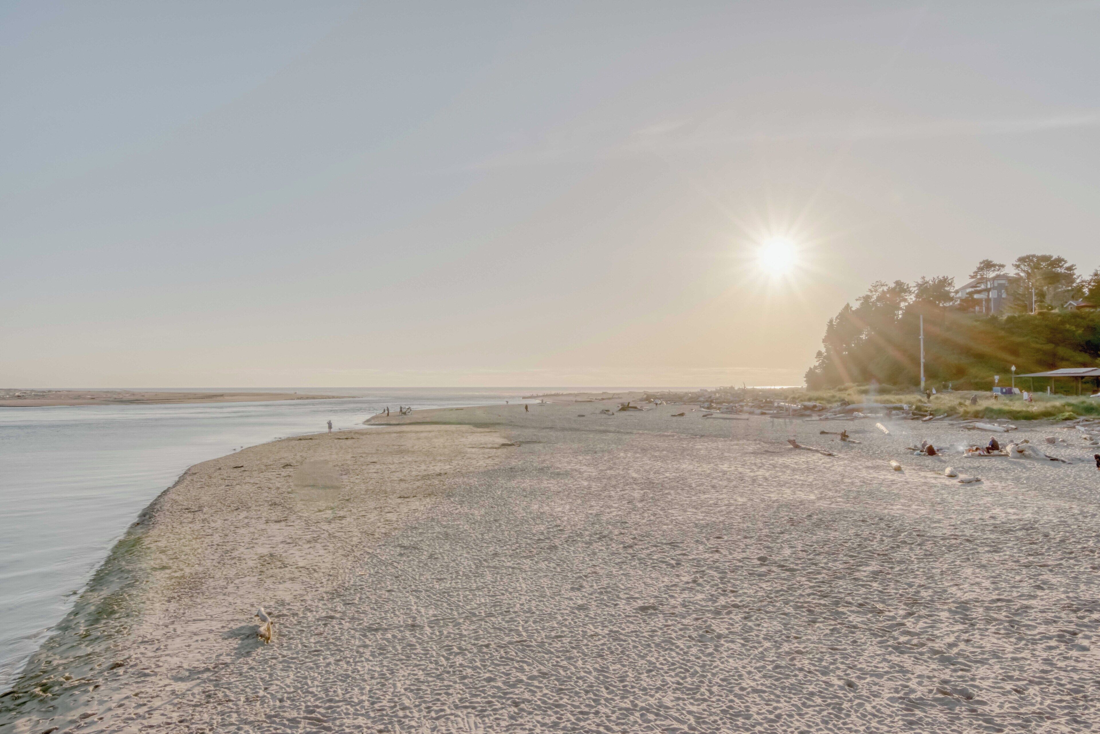 Une plage avec un ciel dégagé, le soleil bas à l’horizon et quelques personnes dispersées le long du rivage.