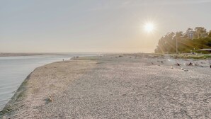 Een strand met een heldere lucht, de zon laag aan de horizon, en enkele mensen verspreid langs de kustlijn.