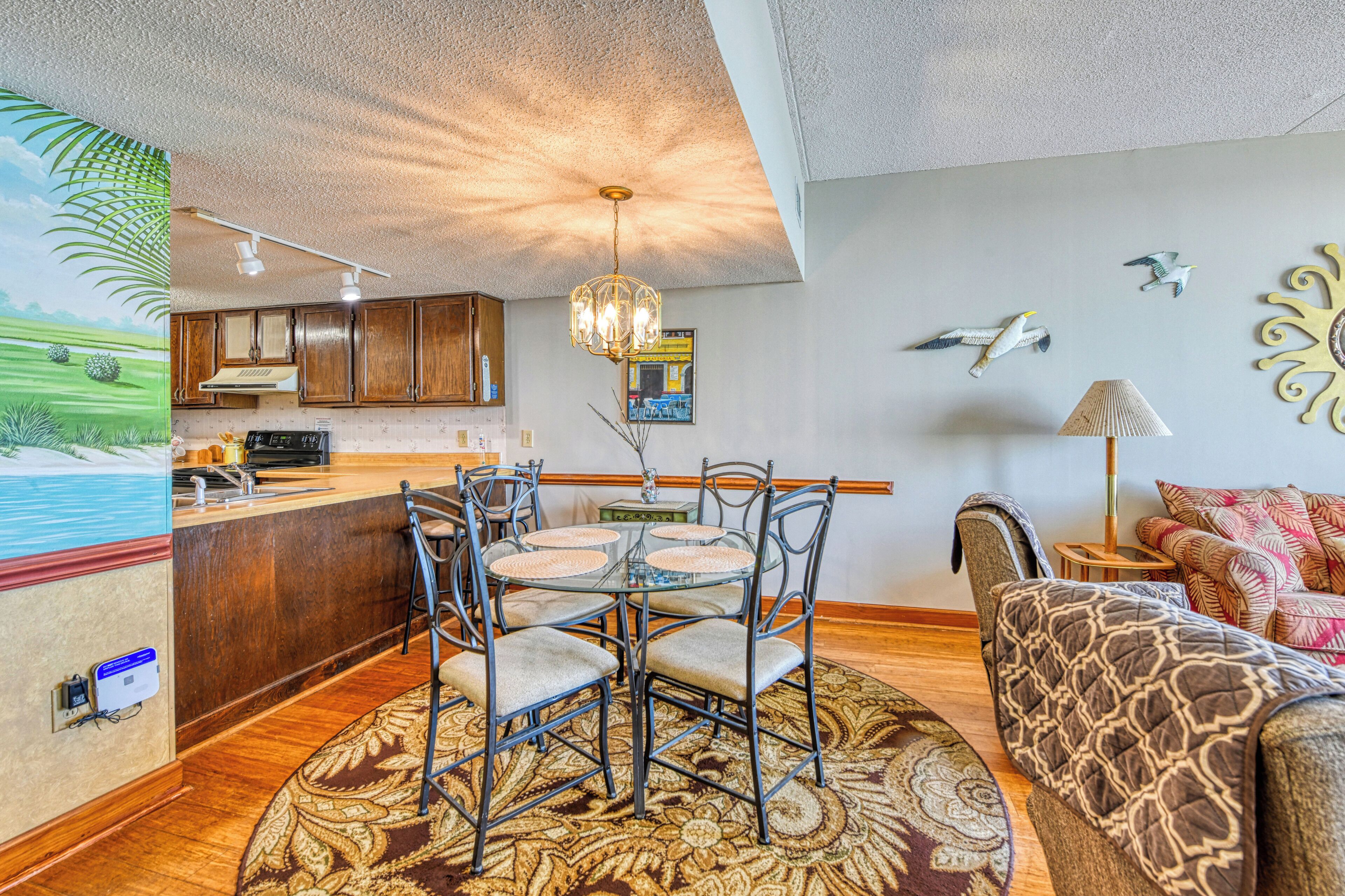A modern kitchen with wooden cabinets, a central island, and a dining area with a glass table and metal chairs.