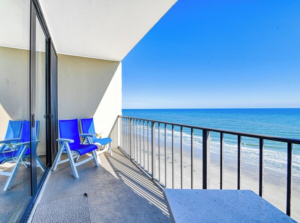 A balcony with a view of the ocean, featuring blue chairs and a glass door.