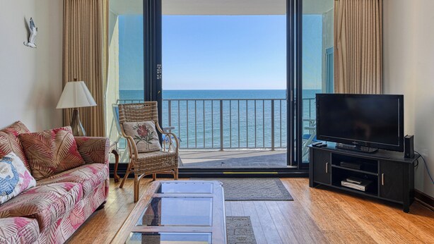 A living room with a sofa, a chair, a TV, and a view of the sea through a balcony. - Horizon East 804 - Two Bedroom, Two Bath Oceanfront Condo (Garden City Beach)