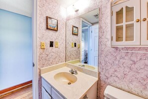 A bathroom with a marble wall, a sink with a mirror, and a cabinet with glass doors.