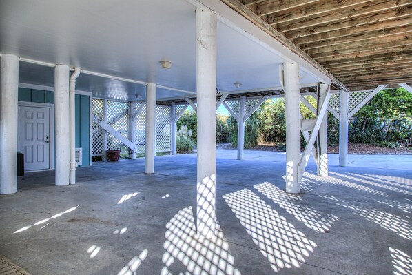 A covered outdoor area with white columns and a wooden ceiling, featuring a door and a lattice fence.