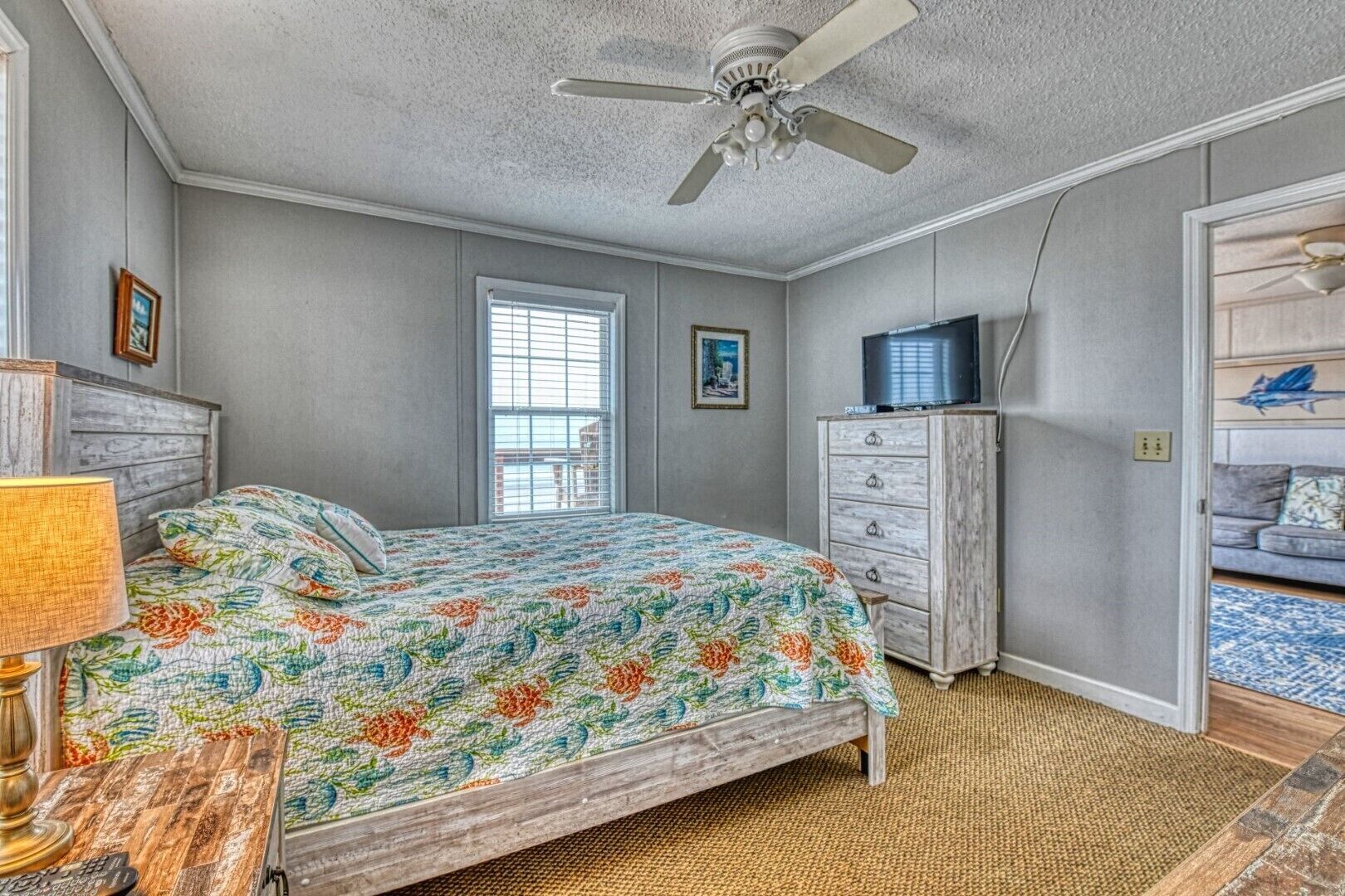 Une chambre à coucher comprenant un lit, une commode, un téléviseur et un ventilateur de plafond.