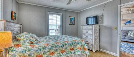 Une chambre à coucher comprenant un lit, une commode, un téléviseur et un ventilateur de plafond.