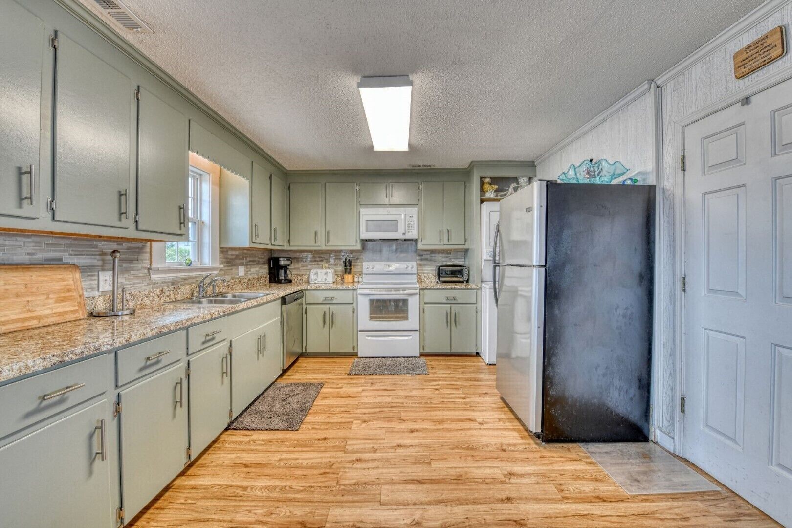 A kitchen with light green cabinets, a granite countertop, a microwave, a toaster, and a refrigerator.