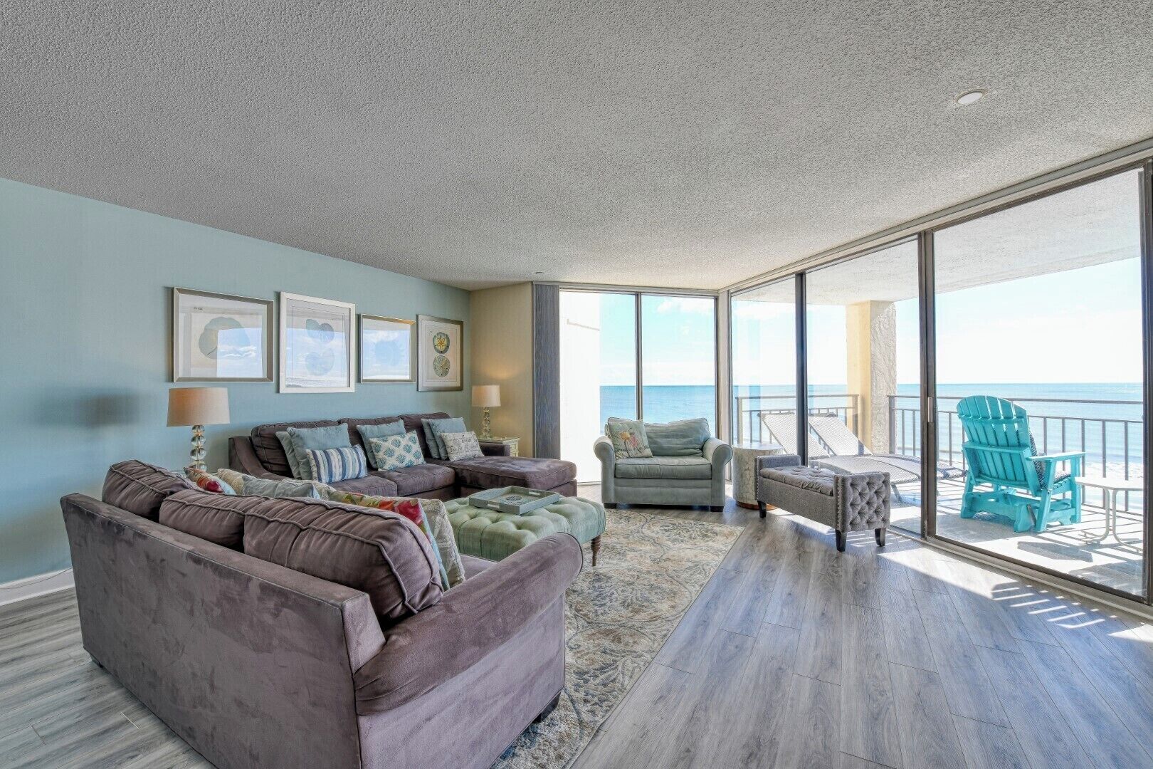 A spacious living area with a large window overlooking the ocean, a sofa set, a small table, and a chair.