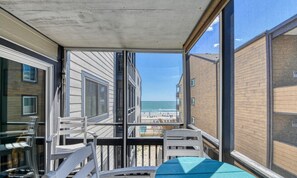 A balcony with a view of the beach, a table, and chairs.