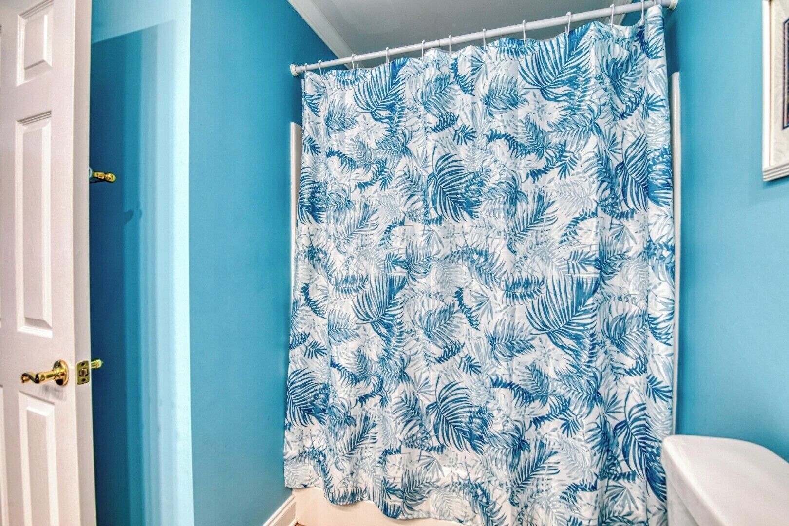 A bathroom with a blue wall, a white door, and a shower curtain with a tropical leaf pattern.