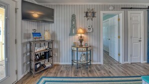 A hallway with wooden paneling, a TV mounted on the wall, a small table with a lamp, and a door leading to another room. - Inlet Summer in Summer House Community (Garden City Beach)