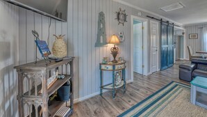 A hallway with wooden flooring, a console table with decorative items, a lamp, and a door leading to another room. - Inlet Summer in Summer House Community (Garden City Beach)