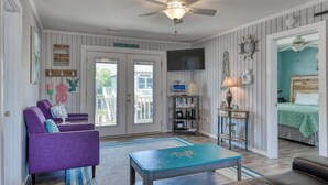 A living room with a ceiling fan, a television, a bookshelf, and a bed with a green bedspread. - Inlet Summer in Summer House Community (Garden City Beach)