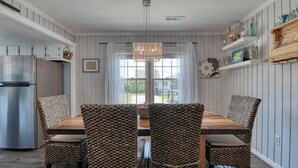 A dining area with a wooden table and woven chairs, a chandelier, and a refrigerator. - Inlet Summer in Summer House Community (Garden City Beach)