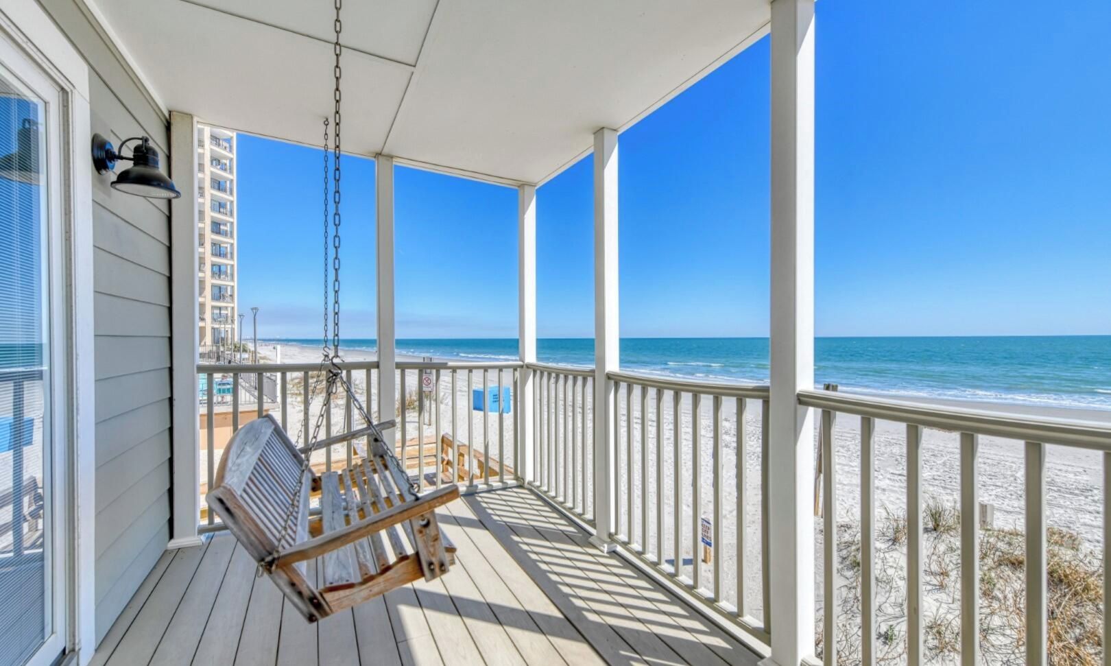 A wooden deck with a swing chair overlooking a beach.