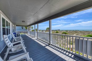 Une vĂ©randa couverte avec des balustrades blanches, une terrasse en bois et une vue sur la plage et lâocĂ©an.