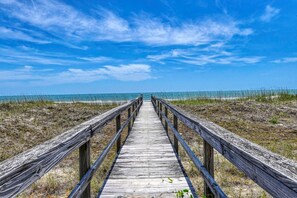 Ein Holzsteig führt zu einem Strand unter blauem Himmel.