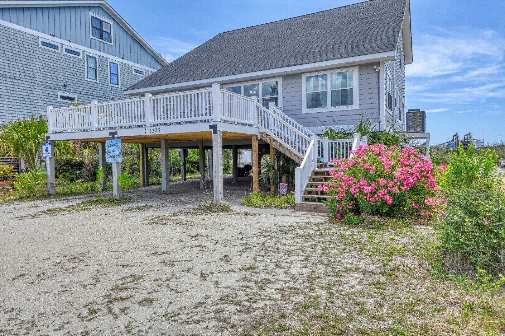 En ejendom ved stranden med en overdækket veranda, en trappe til indgangen og et skilt der angiver havudsigt.