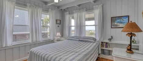 A bedroom with a bed, a ceiling fan, a nightstand, a lamp, a bookshelf, and a view of the outdoors.