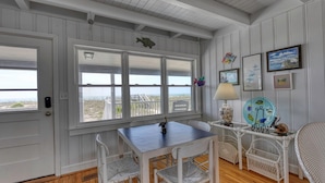 A room with a wooden floor, white walls, a table with chairs, a lamp, and a view of the beach. - Love's A Beach - 5 Bedroom. 4 Bathroom, Oceanfront Dog Friendly Home (Garden City Beach)