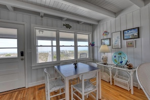 A room with a wooden floor, white walls, a table with chairs, a lamp, and a view of the beach. - Love's A Beach - 5 Bedroom. 4 Bathroom, Oceanfront Dog Friendly Home (Garden City Beach)