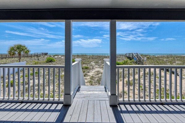 Eine Holzterrasse mit weißen Geländern, die Blick auf einen Strand bietet.