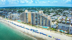 A beachfront hotel with multiple floors, a pool, and a beach area with umbrellas.