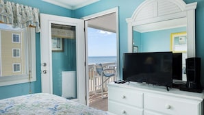 Un dormitorio con cama, cómoda, televisión y vista al océano a través de una puerta abierta.