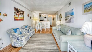 Una sala de estar con sofá, una mesa de comedor con sillas, una zona de cocina y un pasillo que conduce a otra habitación.