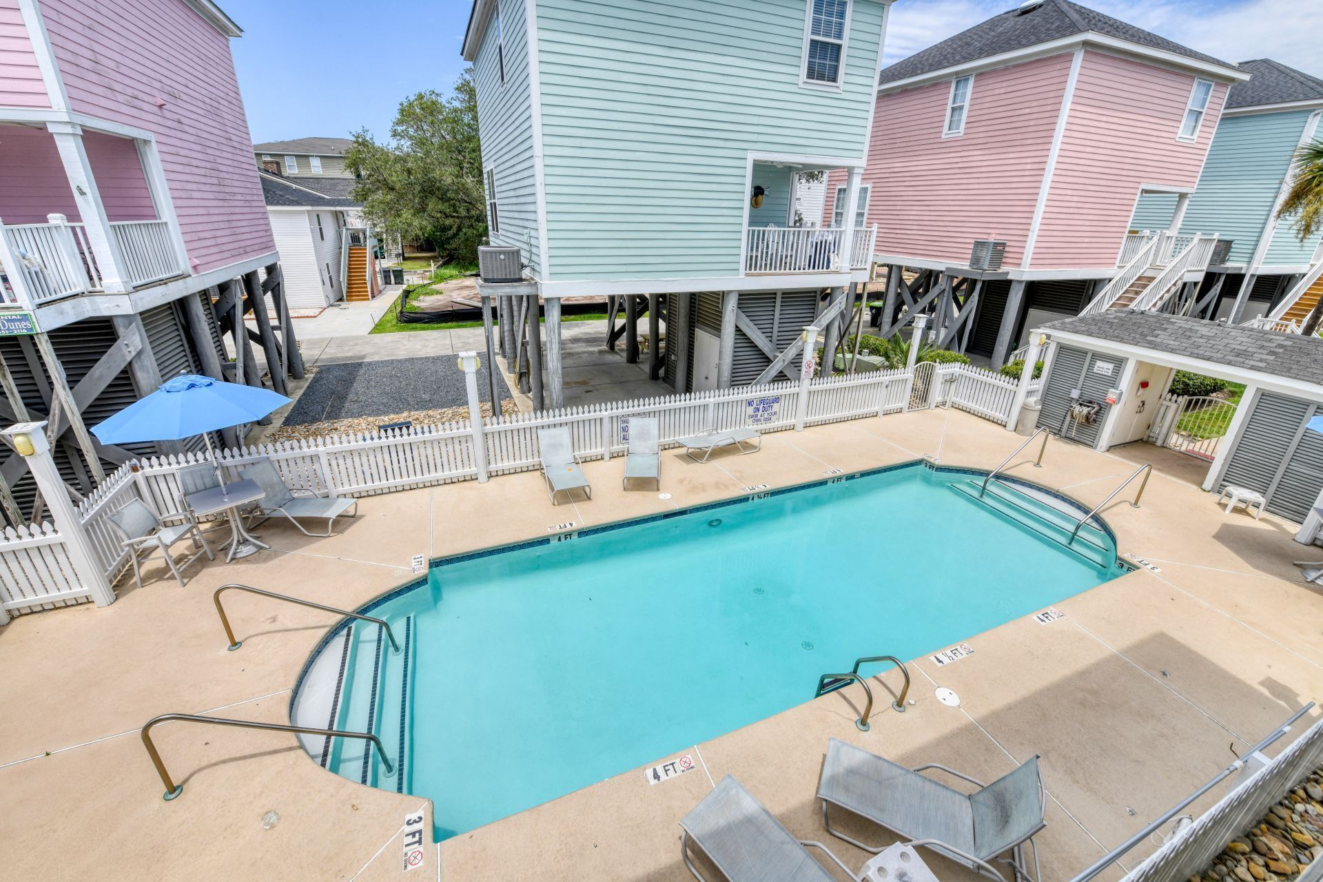 A swimming pool with a white fence, lounge chairs, and a lifeguard stand.
