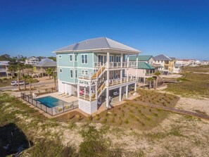 Une maison à plusieurs étages située en bord de mer, dotée d’une piscine, de balcons et d’un passage permettant d’accéder à la plage.