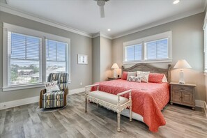 Une chambre à coucher avec un grand lit, deux lampes de chevet, un banc, une chaise et un ventilateur de plafond.