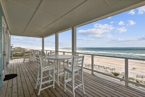 Une terrasse en bois avec des chaises blanches et une table, donnant sur une plage.