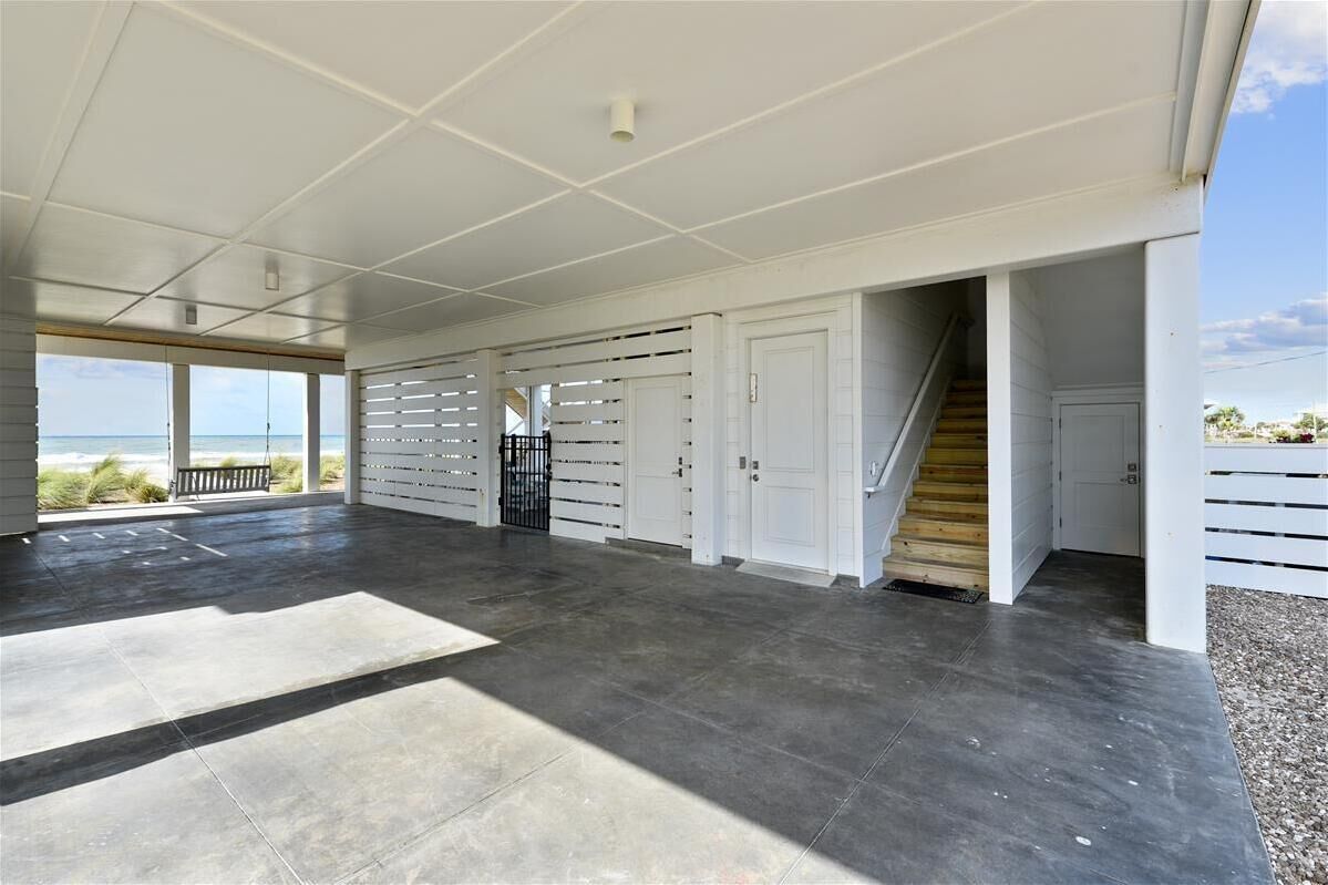 Uma área coberta ampla com vista para o oceano, uma escadaria e uma porta que dá para o interior.