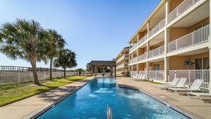 Una piscina con vista despejada a la zona de la piscina, un edificio con balcones y una palmera.
