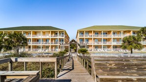 Un resort con edificios de dos pisos, un paseo marítimo de madera que conduce a un área de piscina, y un cielo despejado.