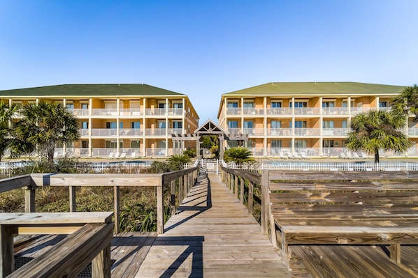 A resort with two-story buildings, a wooden boardwalk leading to a pool area, and a clear sky. - Dauphin Island Beach Club 310 Family Friendly with Incredible Views!!! (Dauphin Island)