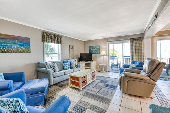 A living room with a sofa, armchairs, a coffee table, and a TV. There is a balcony with a view. - Compass Rose 11, three-bedroom, two-bath condo, ocean front (Garden City Beach)